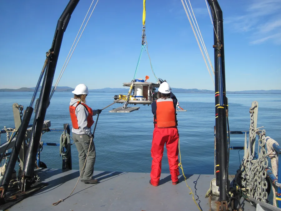 Two researchers deploying an ADCP instrument frame from the deck of a survey vessel in San Pablo Bay