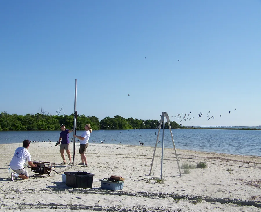 USGS field staff collecting a sediment core using vibracoring equipment on a beach